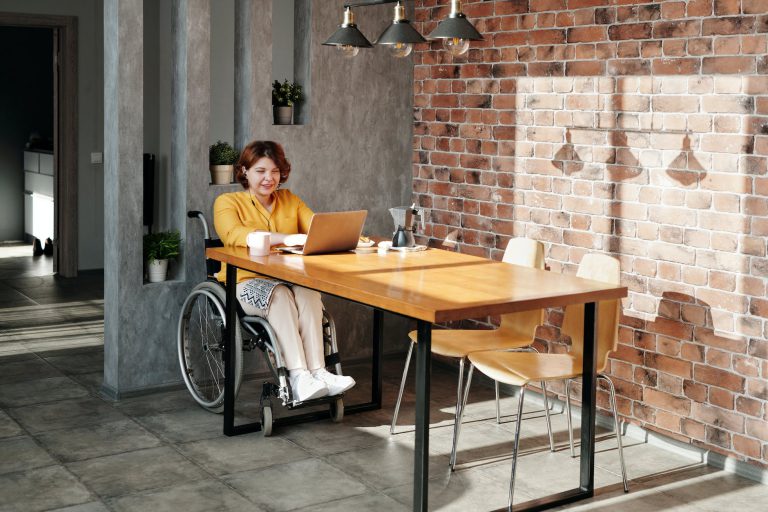 een vrouw in een rolstoel aan tafel met laptop
